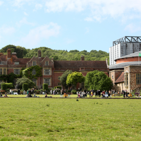 a large building both old and new in the background of a large green lawn