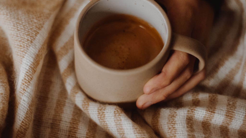 a mug of coffee being held by someone sat under a brown stripe blanket