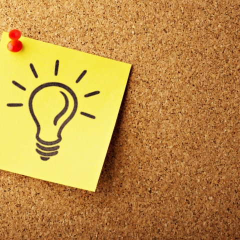 a yellow post it note pinned on a cork board with a lightbulb drawn on