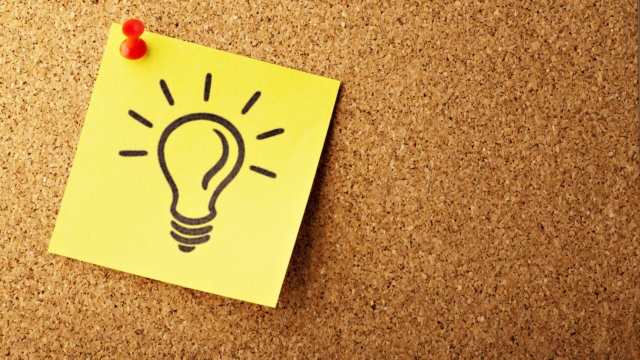 a yellow post it note pinned on a cork board with a lightbulb drawn on