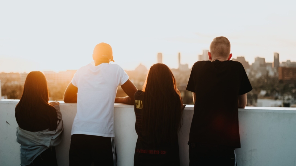 four young people look over a balcony at sunset at a city scape