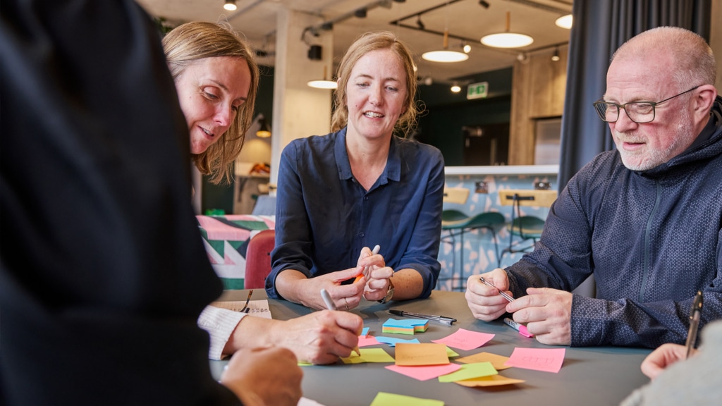 a group of three people sitting around a table full of post-it notes while one woman writes on one