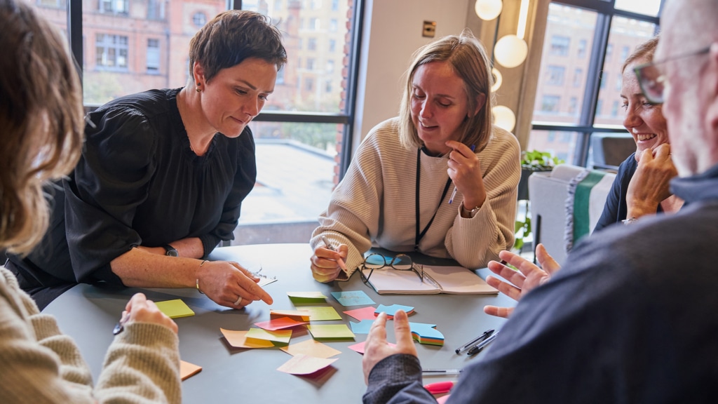 a blonde woman with short hair points at post-it notes with a woman with short brown hair