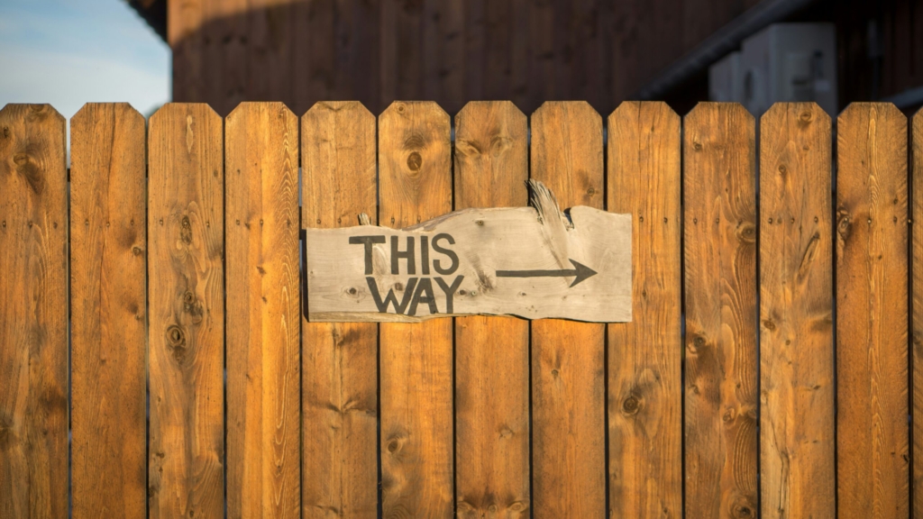 a wooden fence with a rustic wooden sign pointing right with the words, this way