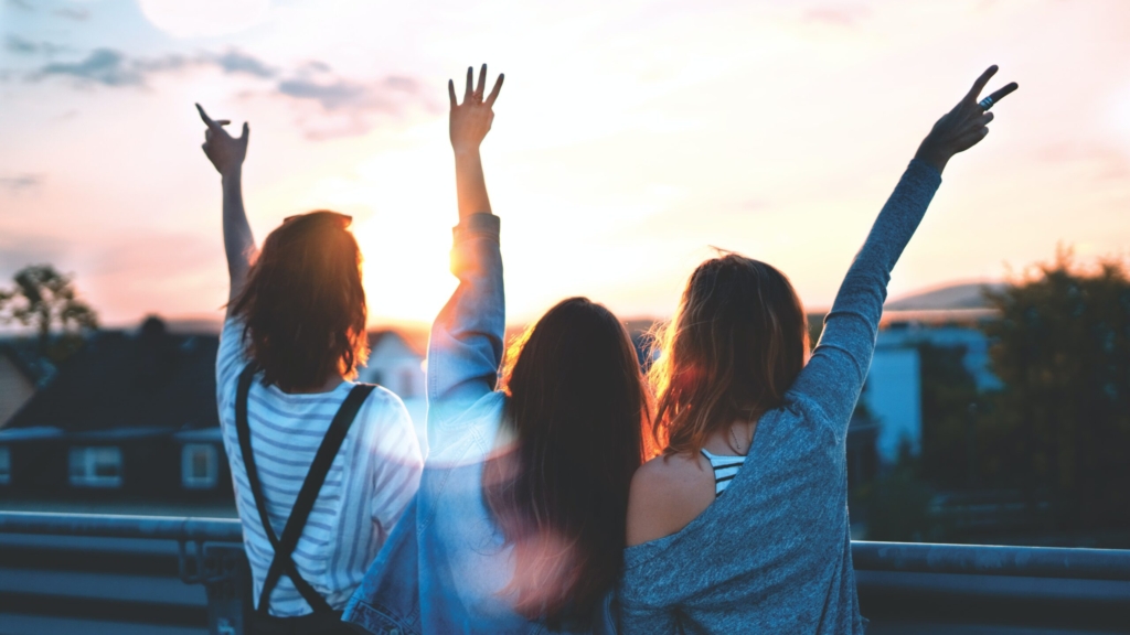three women looking away from the camera holding up their arms, one doing the peace sign