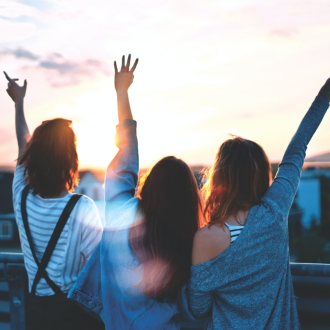 three women looking away from the camera holding up their arms, one doing the peace sign