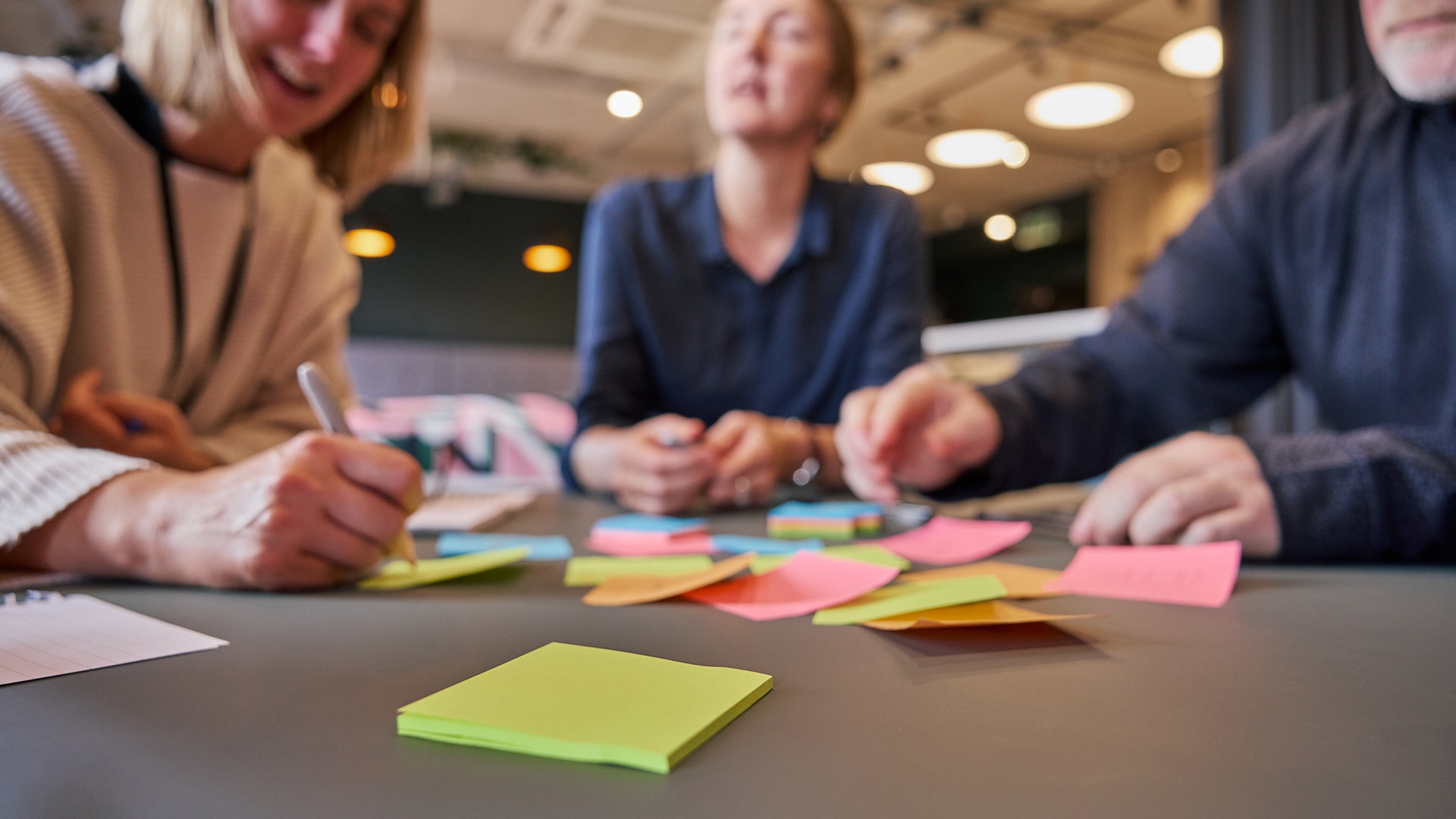 a close up of a green post-it note, there are blurred out people in the background around the table